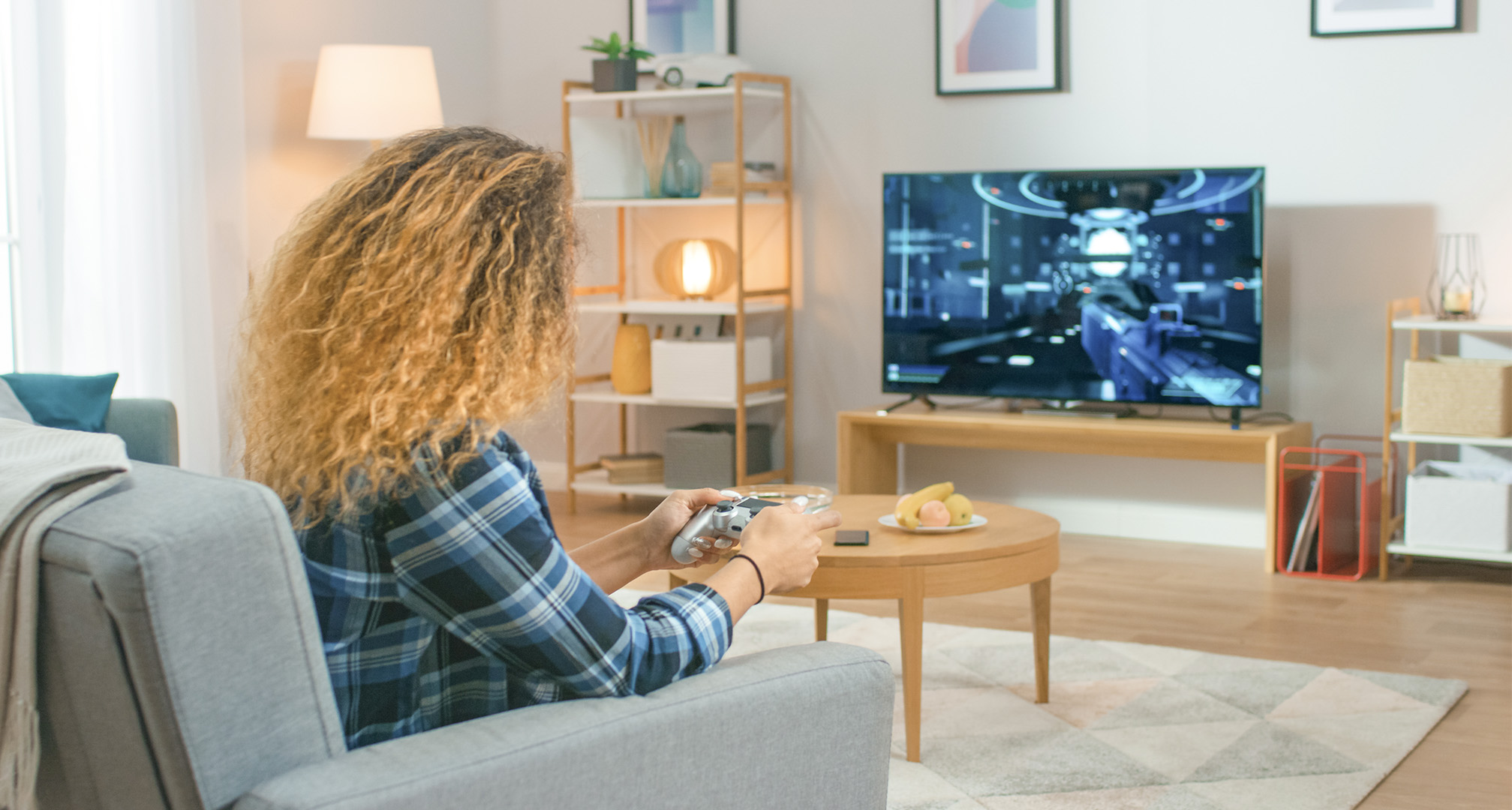 oseba z dolgimi kodrastimi lasmi v dnevni sobi igra videoigre na televiziji